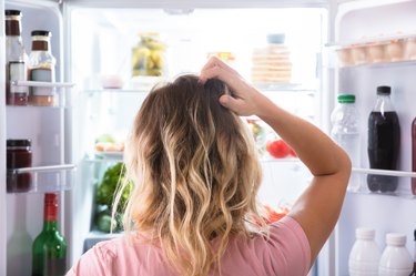 Zbunjena žena bez apetita gleda u hladnjak kod kuće